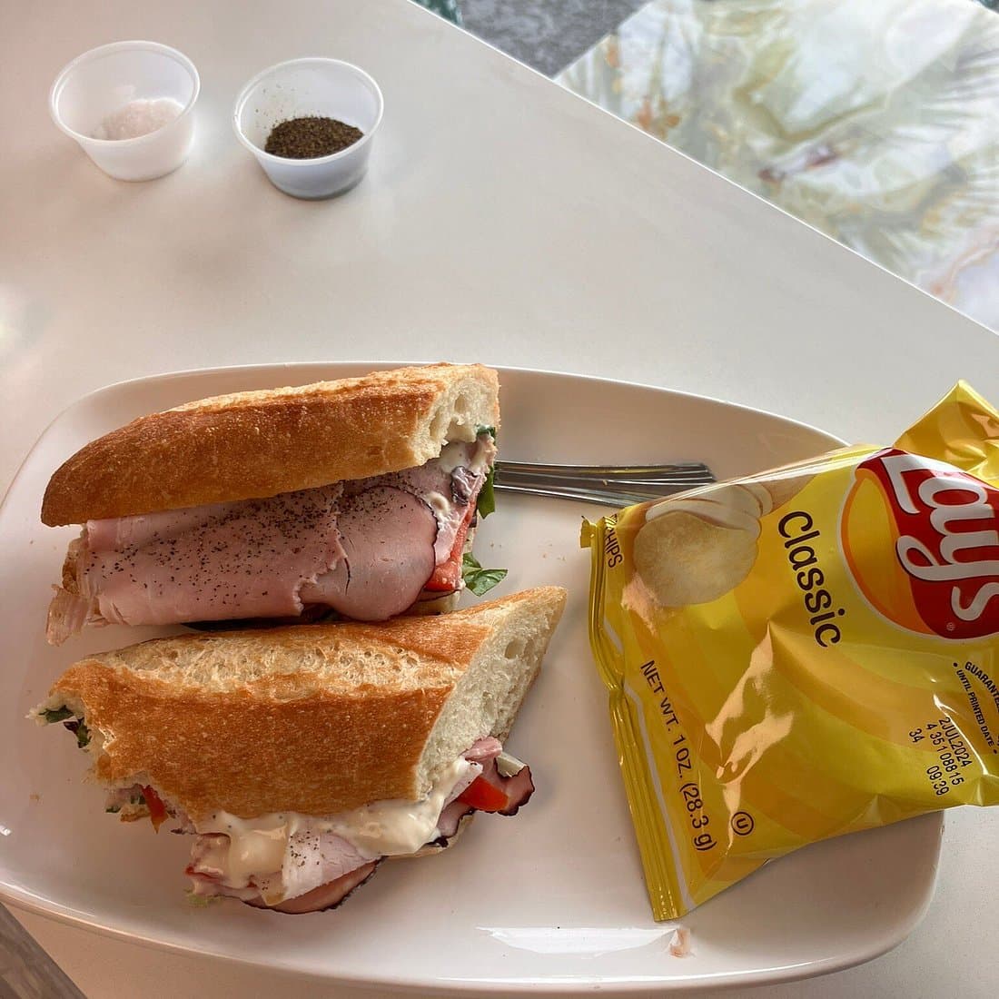 A sliced baguette sandwich plated with chips