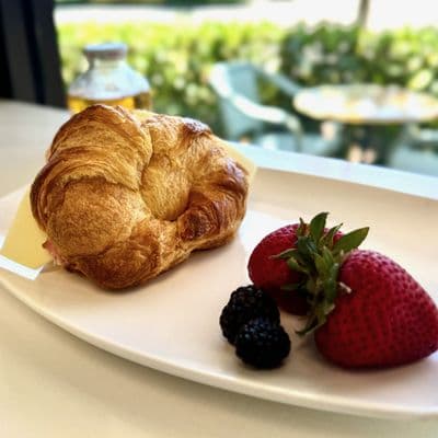 A croissant ham and cheese sandwich plated with strawberries and blackberries